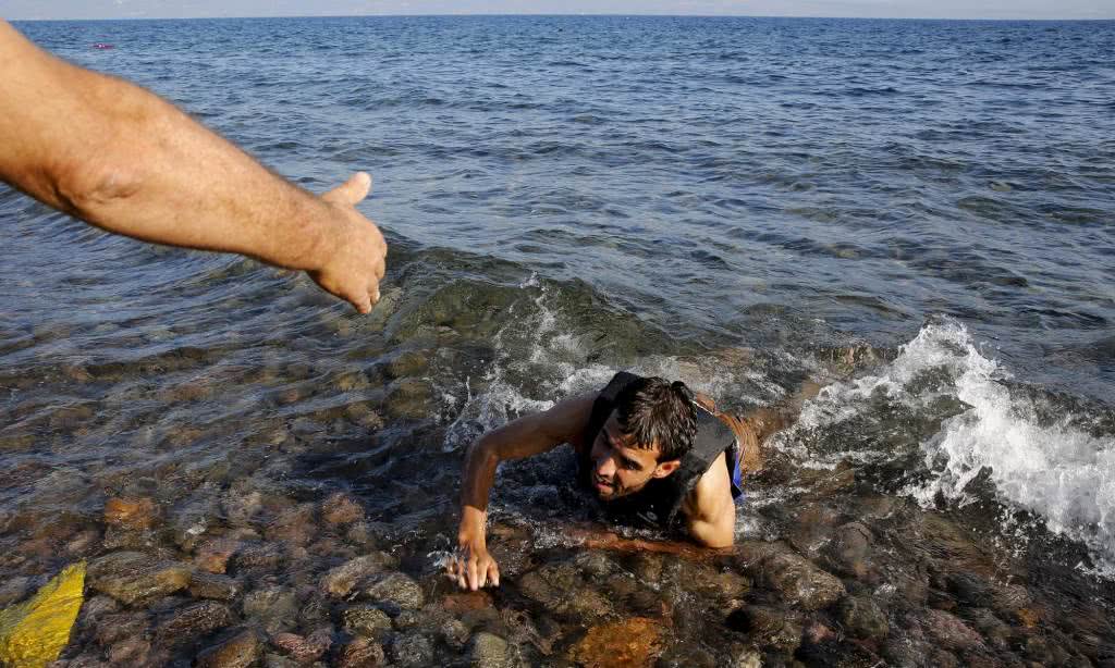 Ένας ντόπιος βοηθάει ένα Σύριο πρόσφυγα καθώς αυτός κολυμπά προς τη στεριά εξαντλημένος.