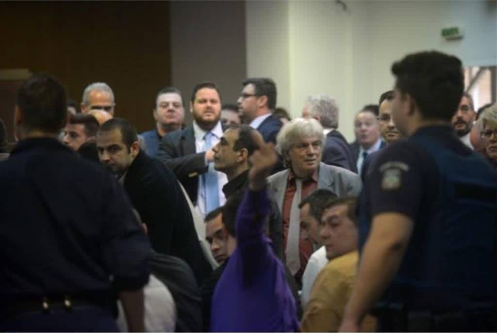Σήμερα στη δίκη της Χρυσής Αυγής. Ο Καζαντζόγλου, κατηγορούμενος για άμεση συνέργεια στην ανθρωποκτονία του Παύλου Φύσσα, κάνει κωλοδάκτυλο προς την οικογένεια του θύματος.